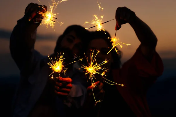 Party, event and holiday concept - man and woman fooling around with sparklers against sunset sky