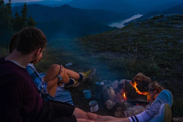 Genç çift kamp ateşinde dinleniyor ve kahve içiyorlar. — Stok fotoğraf