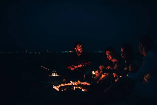 Amigos disfrutando de música cerca de la fogata por la noche —  Fotos de Stock