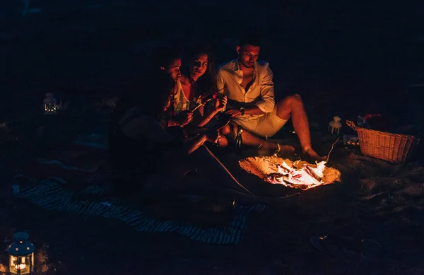 Şenlik ateşinin yanında elini ısıtan mutlu insanlar. Gece vakti. — Stok fotoğraf