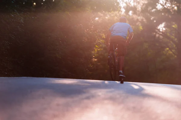 Muž cyklista na kole při západu slunce na silnici přes hluboké wo — Stock fotografie
