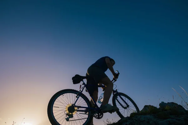 Silueta mužského cyklistického bikera na kole do kopce o — Stock fotografie