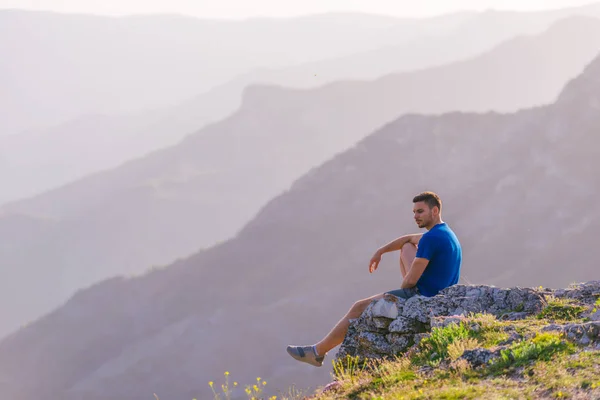 Homem aventuroso sentado no topo de uma montanha e apreciando o ser — Fotografia de Stock
