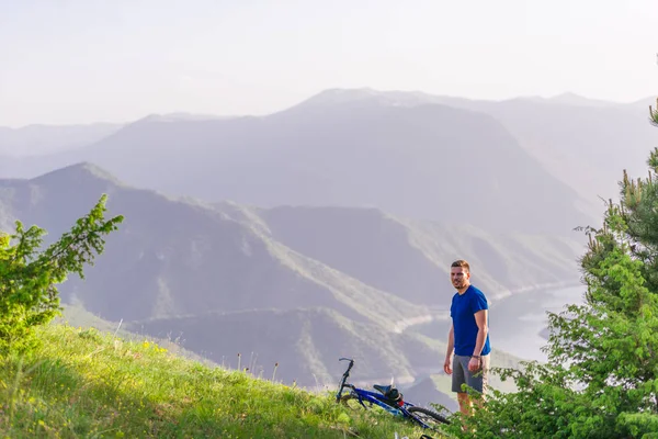 Mountainbiker drinkt water terwijl hij bij een groen dal staat en — Stockfoto