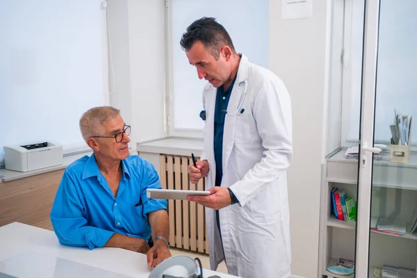 Kaukasischer Arzt mittleren Alters erklärt seinem älteren Patienten seine — Stockfoto