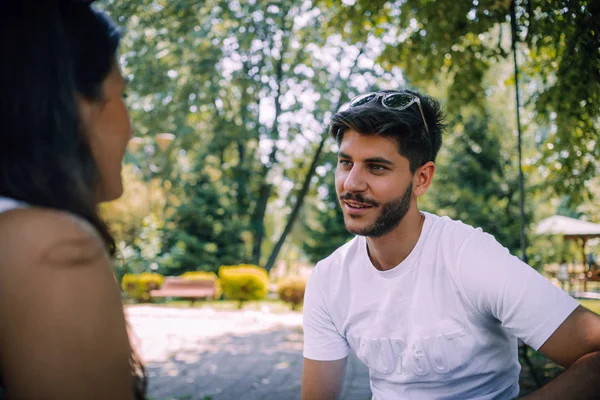 Chica hablando con un amigo en el parque mientras está sentado en el banco — Foto de Stock