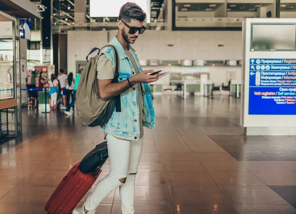 Joven Tirando Maletas Interior Sala Del Aeropuerto Mientras Usa Teléfono —  Fotos de Stock