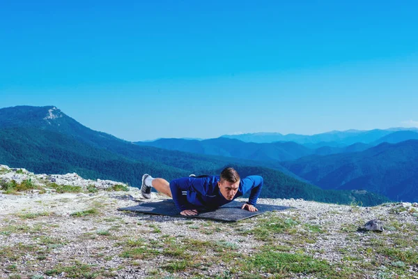 强壮英俊的金发运动员在山顶上做俯卧撑 同时欣赏山谷中湖面的迷人景色 — 图库照片