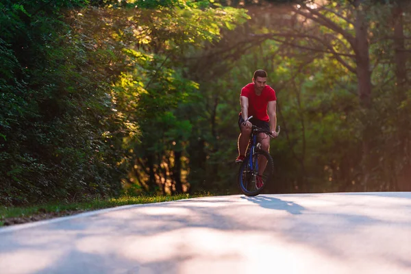 Férfi kerékpáros biciklizik naplementekor egy mély úton. — Stock Fotó