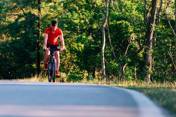 Fit bisikletçi doğada boş bir yolda bisikletini sürüyor. — Stok fotoğraf