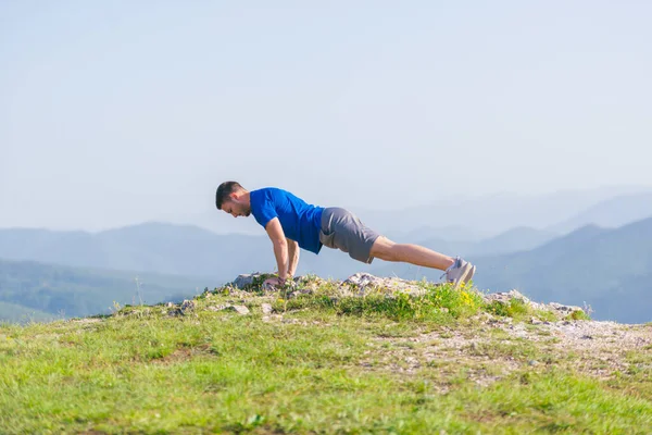 一个年轻的适合男性运动员正在户外做俯卧撑在悬崖上 — 图库照片