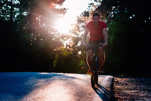 Maschio ciclista in sella alla sua moto al tramonto su una strada attraverso profondo wo — Foto Stock