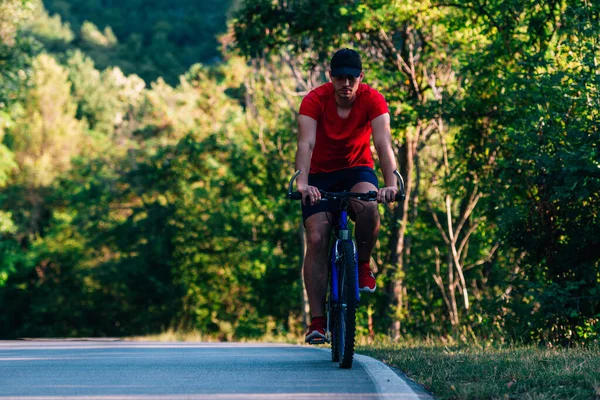 Fit bisikletçi doğada boş bir yolda bisikletini sürüyor. — Stok fotoğraf