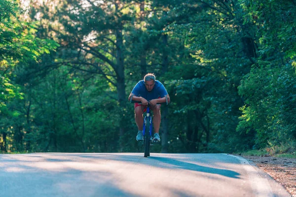 Ciclista de más edad a mediados de los años 40 que conduce una bicicleta en una carretera a través de la carretera. —  Fotos de Stock