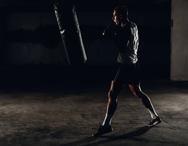 Silhouette male boxer hitting a huge punching bag at a boxing studio. Man boxer training hard