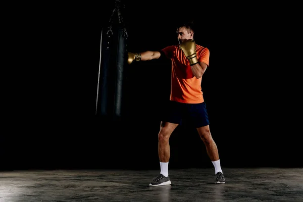 Silhouette male boxer hitting a huge punching bag at a boxing studio. Man boxer training hard