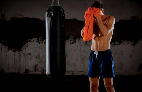 Man in the garage after workout. He is sweaty, exhausted and wiping the head with a shirt