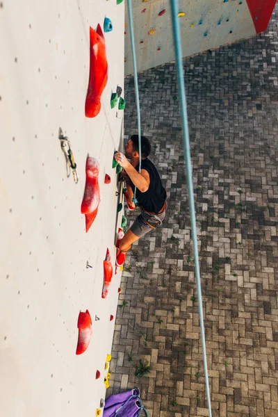 Homem esportivo sobe na parede de rocha artificial — Fotografia de Stock