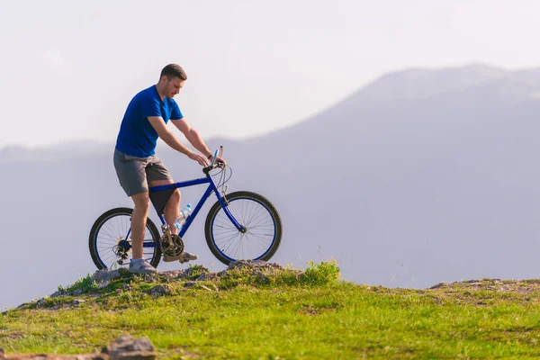 Fit mountain biker riding his bike through green grass on top of — Stock Photo, Image