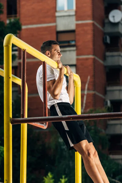 Fuerte joven en forma hombre haciendo pull-ups en un bar en el parque de la ciudad —  Fotos de Stock