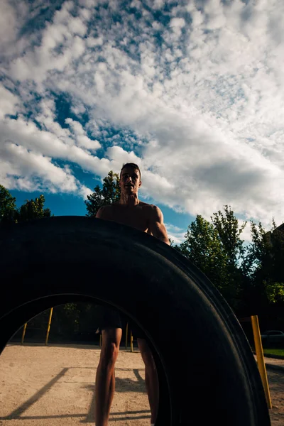 Bez koszuli człowiek przerzucanie ciężkie opony na crossfit siłowni przed zachmurzenie — Zdjęcie stockowe