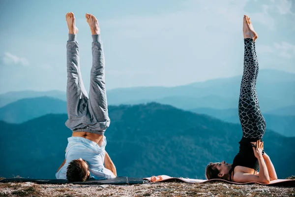 Jovem casal está praticando ioga no lago da montanha — Fotografia de Stock