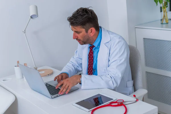 Άνδρας σοβαρός καυκάσιος γιατρός κάθεται στο γραφείο του μόνος και ου — Φωτογραφία Αρχείου