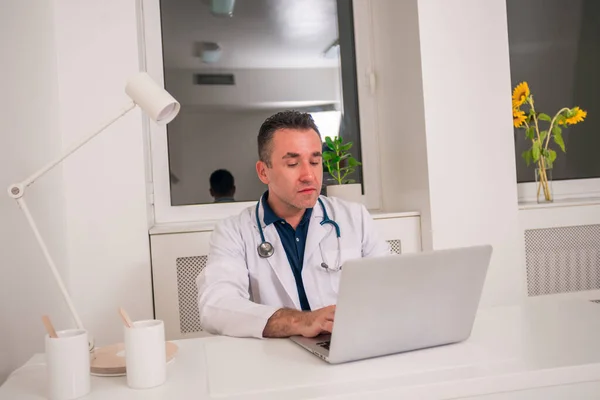 Retrato del médico especialista sentado en una silla en su escritorio whi —  Fotos de Stock