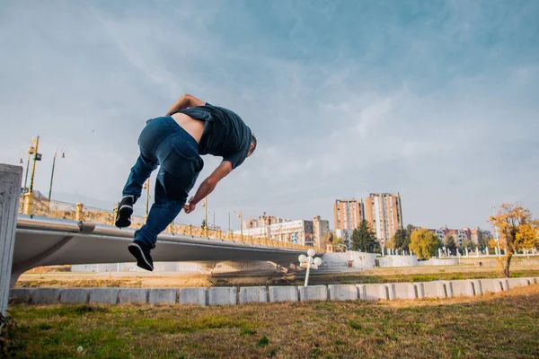 Hombre cuidadoso debajo de las nubes blancas haciendo entrenamiento de parkour. —  Fotos de Stock