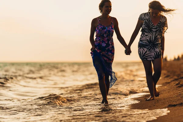 Vrouw is hand in hand, terwijl lopen op nat zandstrand bij zonsondergang — Stockfoto