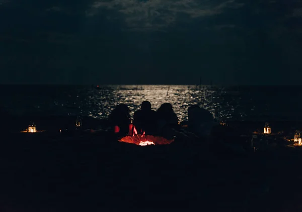 Amigos pela fogueira relaxando durante a noite enquanto assiste o lago — Fotografia de Stock