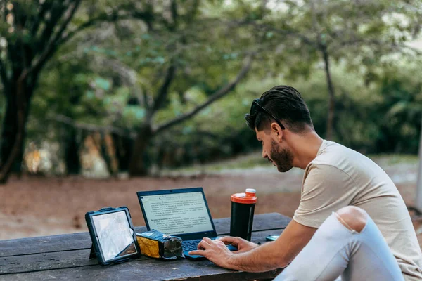 Junger Mann arbeitet im Park an seinem Laptop — Stockfoto
