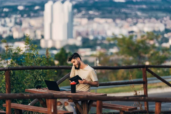 Hombre sentado al aire libre y trabajar en el ordenador portátil contra paisaje urbano —  Fotos de Stock