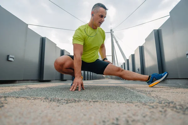 Older well built man in activewear stretching out his legs before running