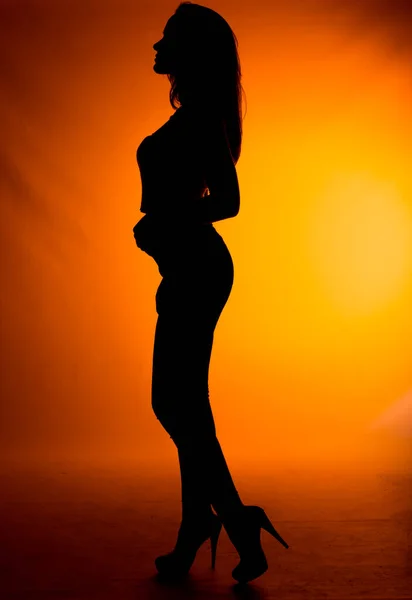 ポートレートの魅力的なトレンディーなスキニー女の子で黒トップとジーンズポーズで夕日の色の壁 — ストック写真