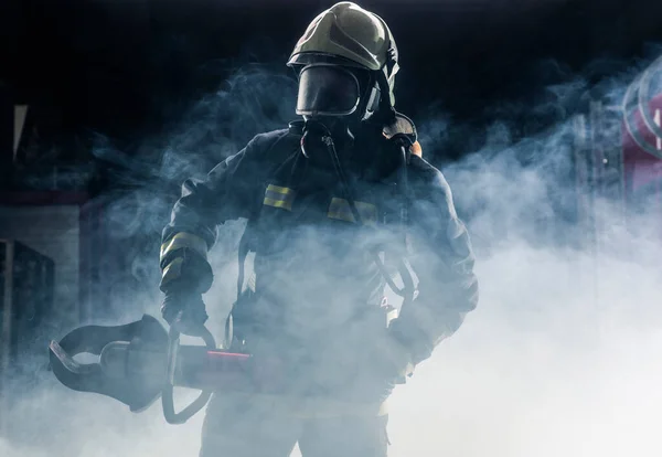 一个身穿消防员制服和头盔的消防员的画像 黑黑的背景 烟雾弥漫 蓝光闪烁 — 图库照片