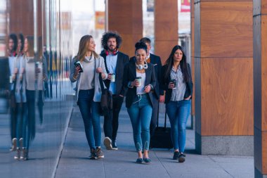 Full length of a group of colleagues in casual businesswear discussing business while walking at office hall clipart