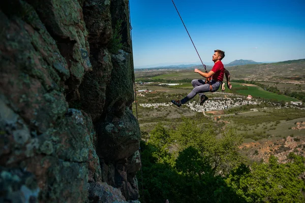 若い男は日の出に山のある谷の岩壁に登る — ストック写真