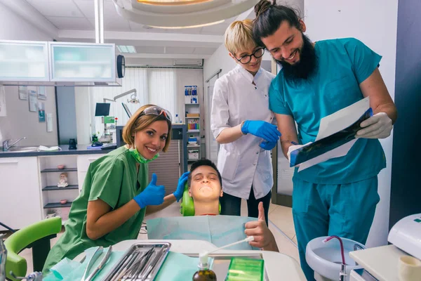 10代の男の子の患者にX線写真を示す男性歯科医の肖像画一方 彼の笑顔の女性の同僚は彼を助けている — ストック写真