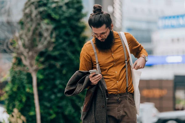 Young caucasian guy clothed in a fashionable costume checking his smart phone
