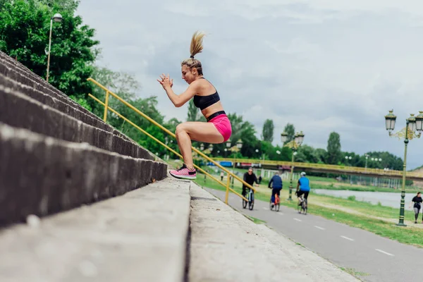 健康的なアスリートにフィット 階段を飛び降りるタイトなスポーツウェアの美しい女性 非常にやる気に見えるながらジョギングの前に暖まる — ストック写真