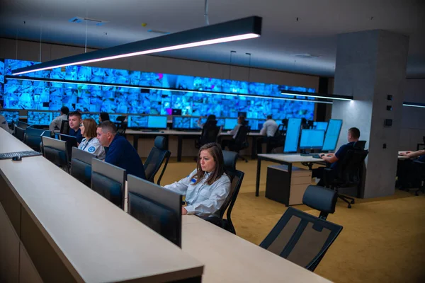 Group of Security data center operators (administrators) working in a group at a CCTV monitoring room while looking at multiple monitors ( computer screens)