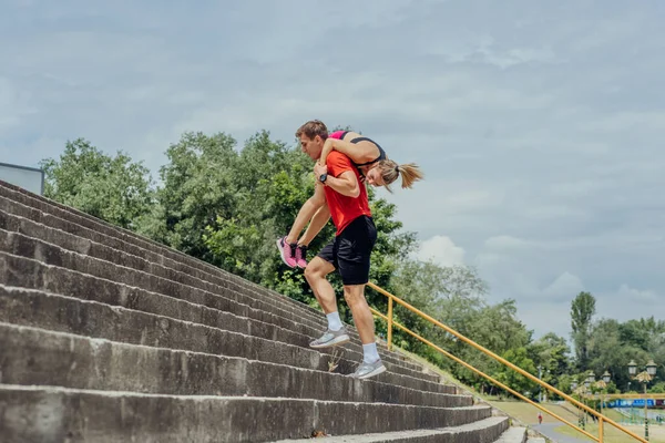 階段を駆け上がりながら肩に女性のトレーニングパートナーを運ぶ男性選手 — ストック写真