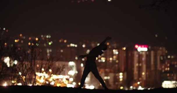 一个男舞蹈演员的轮廓在夜晚在山上的城市灯光前跳舞 镜头低调 — 图库视频影像