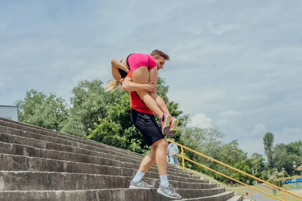 階段を下りながら肩に女性のトレーニングパートナーを運ぶ男性アスリート — ストック写真