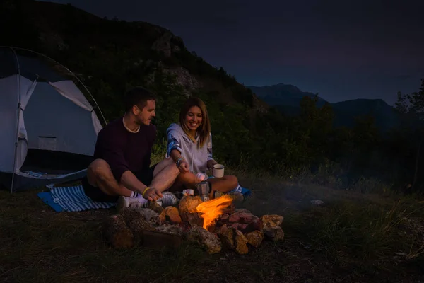 Młoda Para Relaksujący Przy Ognisku Rosting Marshmallows Podczas Picia Kawy — Zdjęcie stockowe