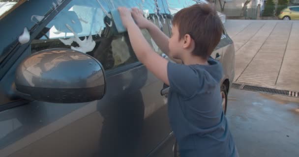 Junge Wäscht Auto Vor Der Garage Mit Schwamm Und Seifenblasen — Stockvideo