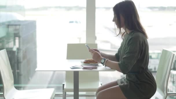 Joven morena comer un sendwich en la moderna cafetería del aeropuerto — Vídeos de Stock