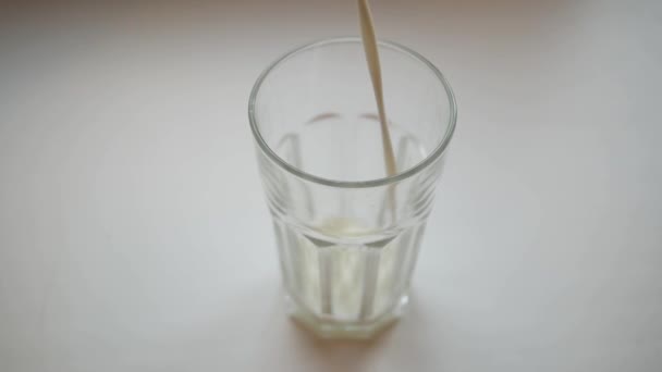Fotografía en cámara lenta de verter un vaso de leche sobre un fondo blanco . — Vídeos de Stock