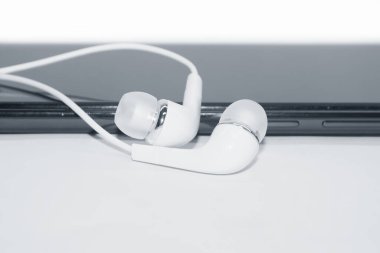  Akıllı telefonun üzerinde bir çift beyaz kulaklık var. Beyaz arka planda izole edilmiş..